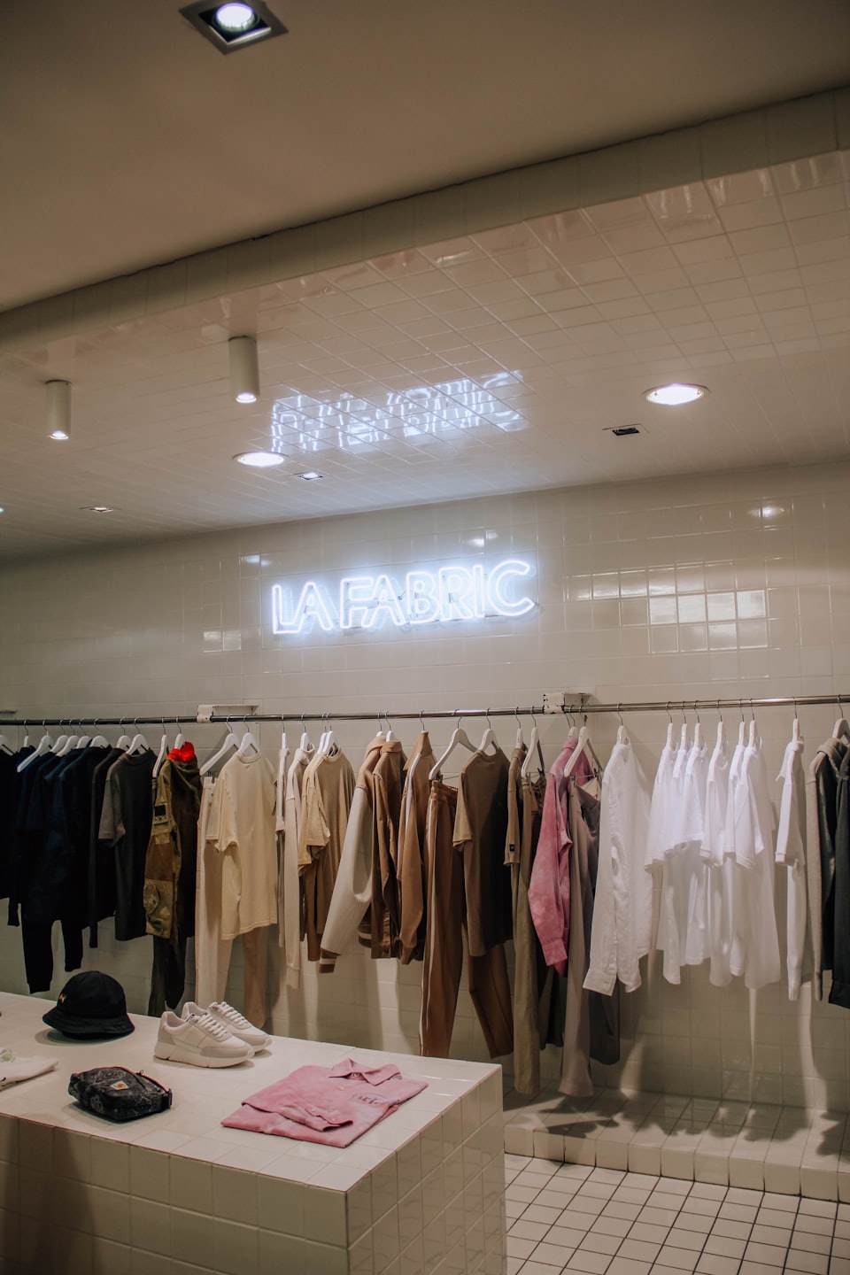 Minimalist clothing store displaying garments and accessories under a neon sign.