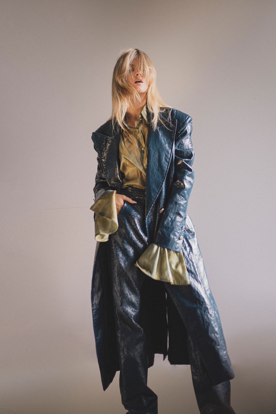 Woman wearing a teal leather coat and pants posing in studio.