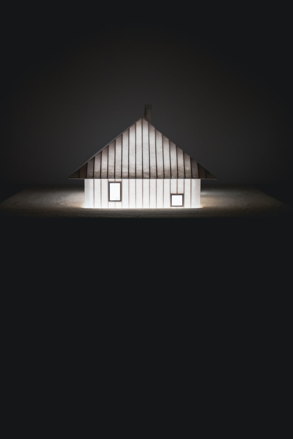 Glowing minimalist house model sitting on a textured surface.