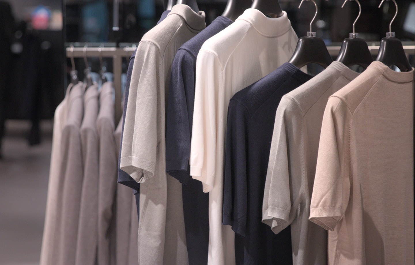 Neutral colored knit shirts hang on a metal clothing rack.