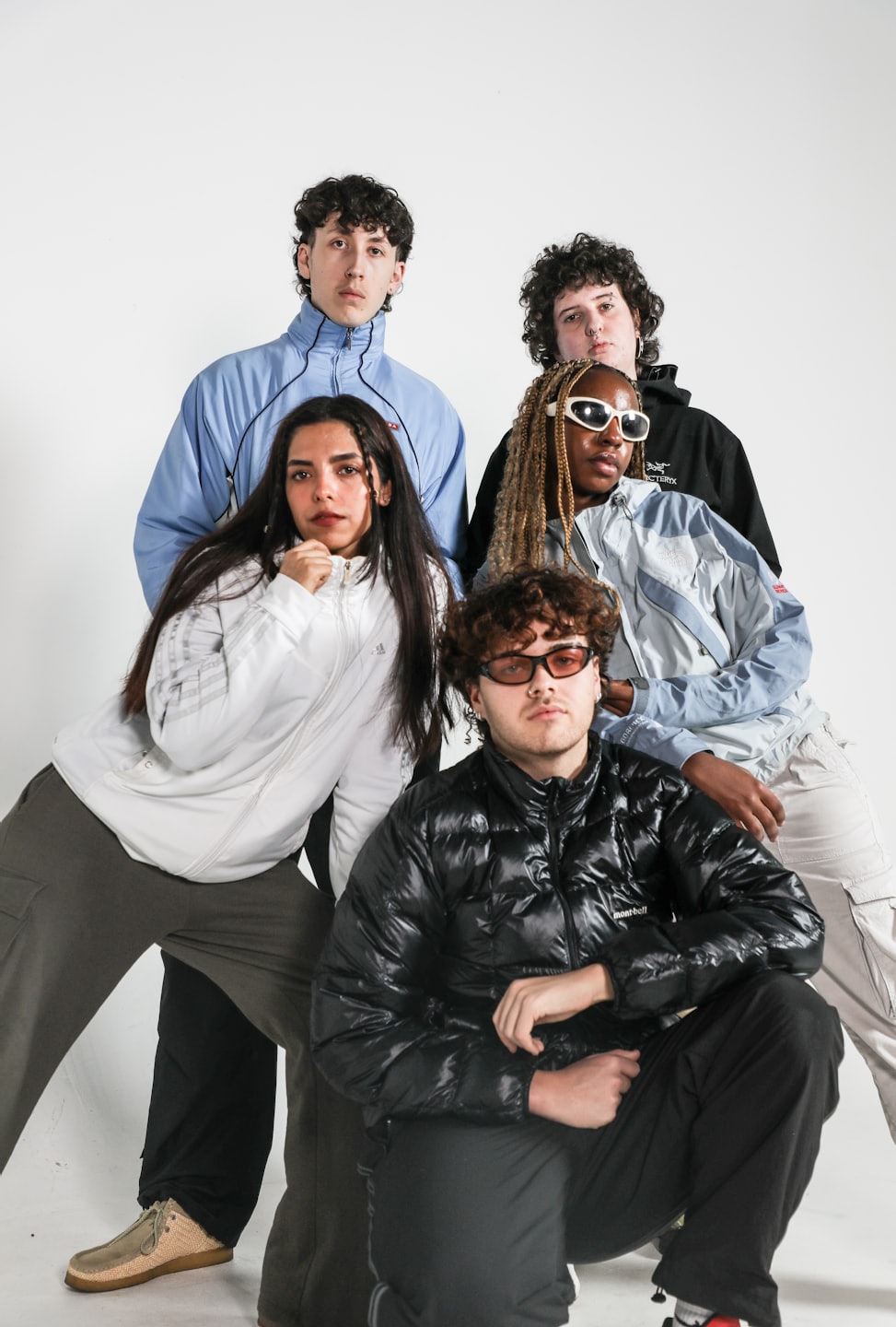 Five young adults in streetwear pose in a bright studio.